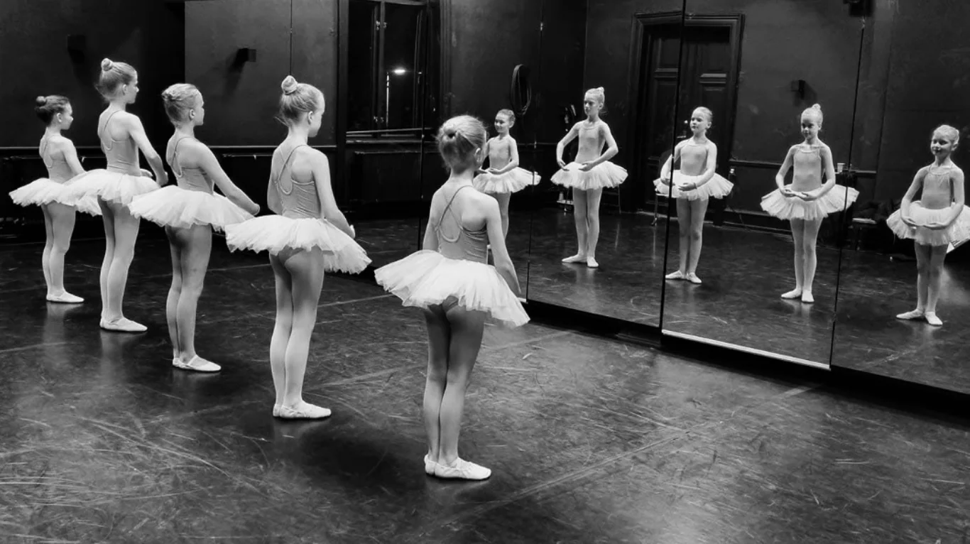 Unge balletdansere i hvide tutuer træner foran spejlvæggen i Spejlsalen