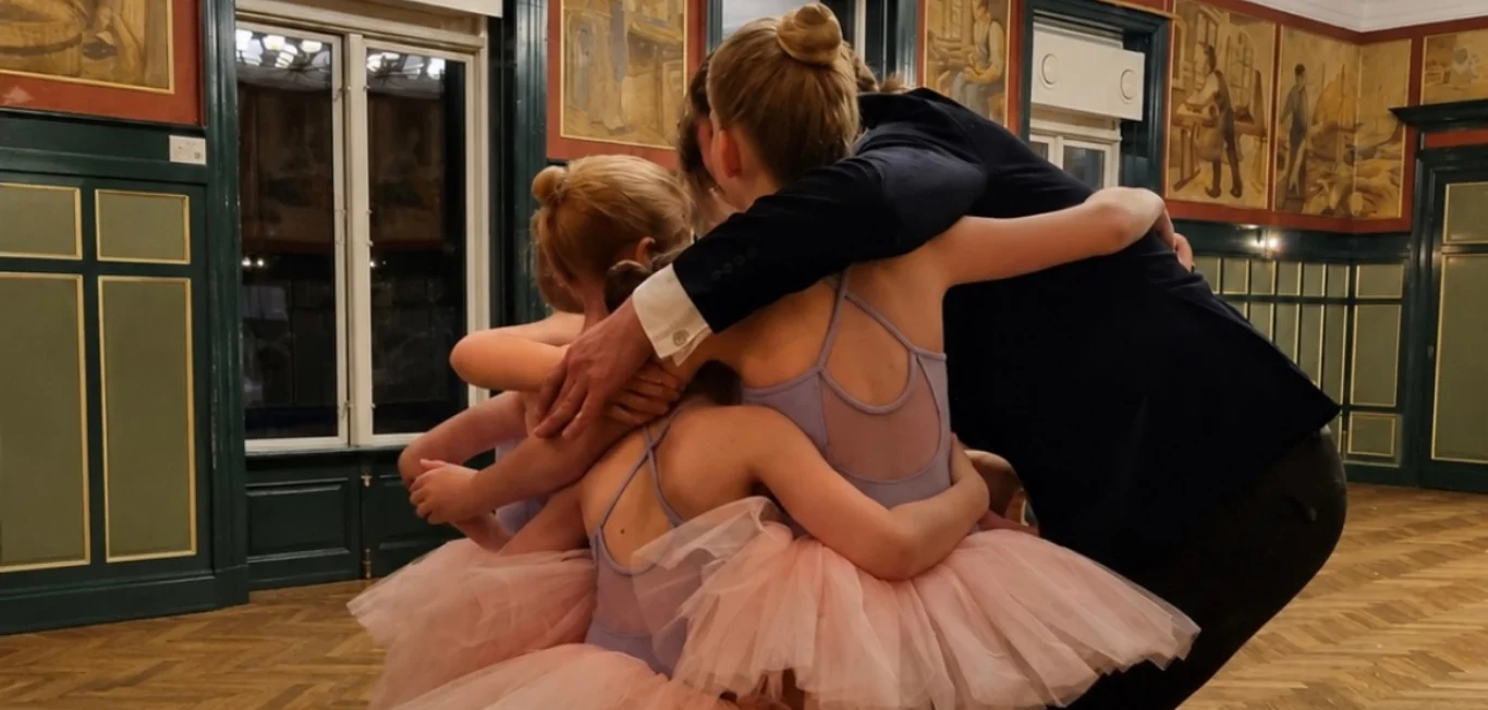 Underviser omfavner en gruppe små balletdansere i rosa tutuer efter undervisning