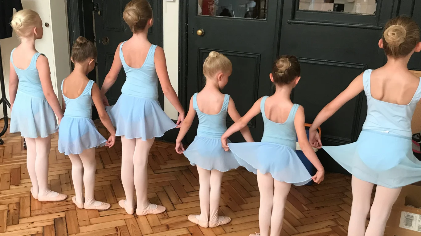Børn i lyseblå balletdragter står på række hånd i hånd